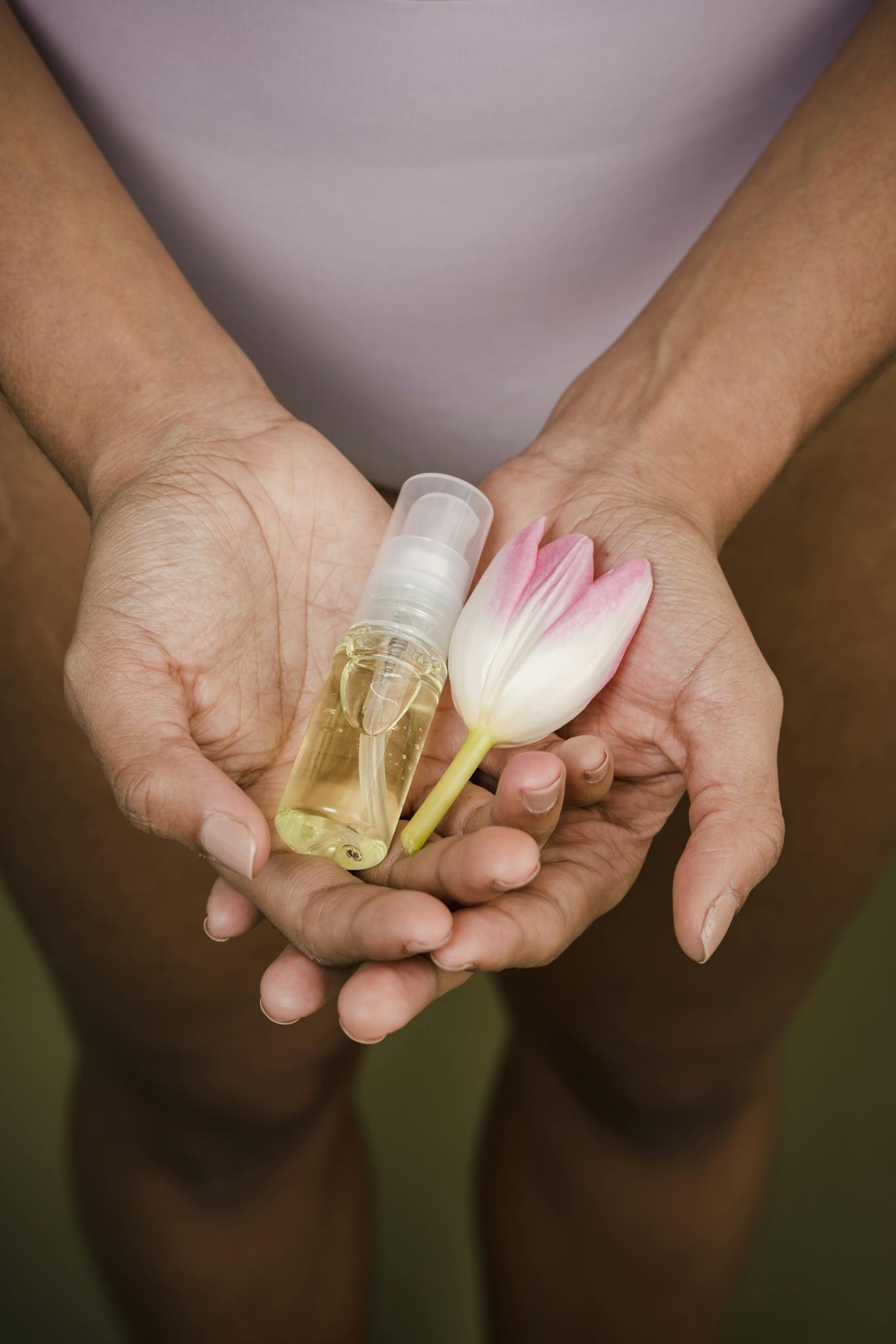 Close-up of hands holding a bottle of essential oil and a tulip, symbolizing natural skincare.