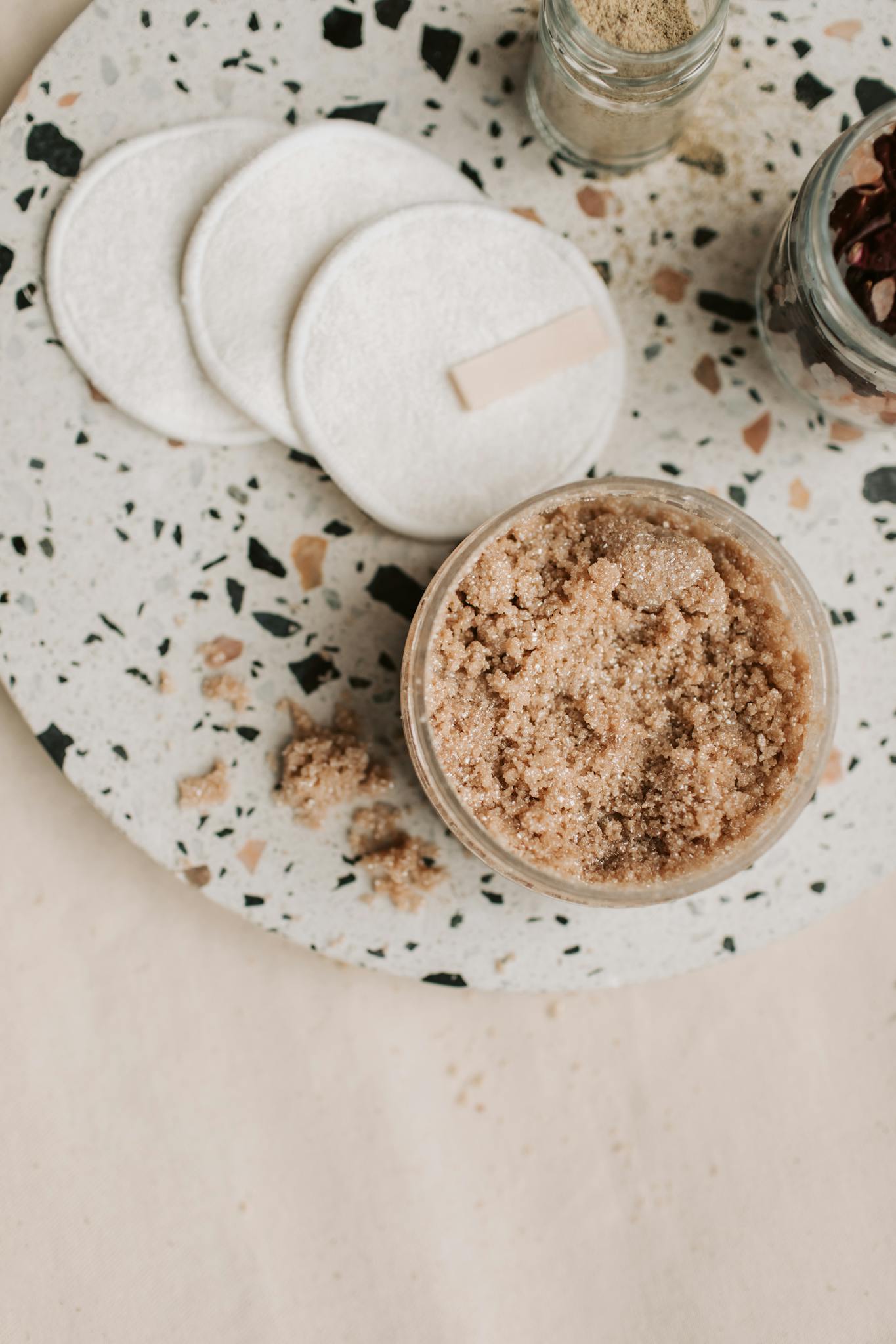 Eco-friendly brown sugar body scrub with cotton pads on terrazzo surface.